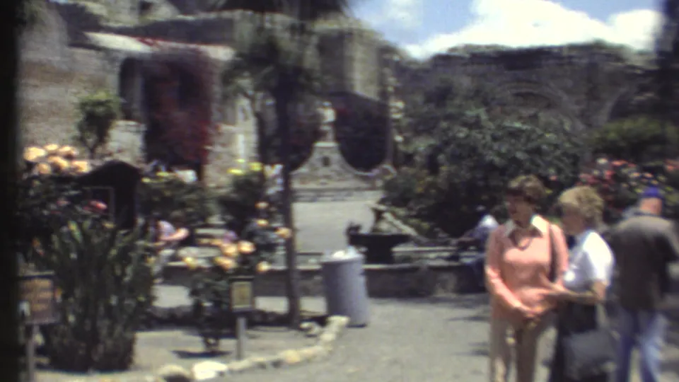 1972 Grand Canyon courtyard scene with visitors near flowering plants, trees, benches, and weathered stone structures.