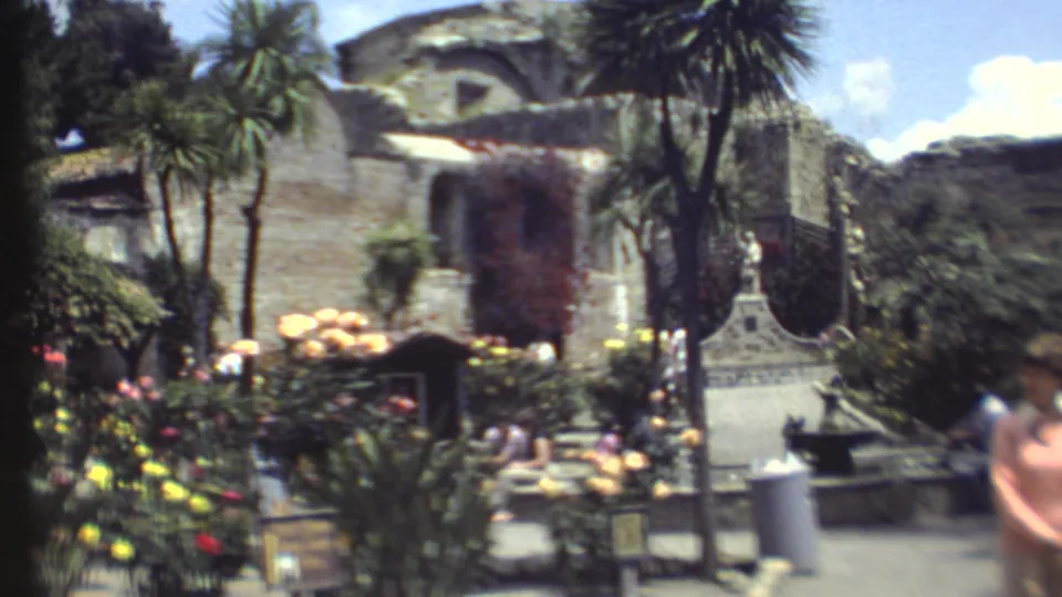 1972 8mm view of a Grand Canyon landscaped courtyard with bright flowers, palm-like trees, benches, and stone facades.
