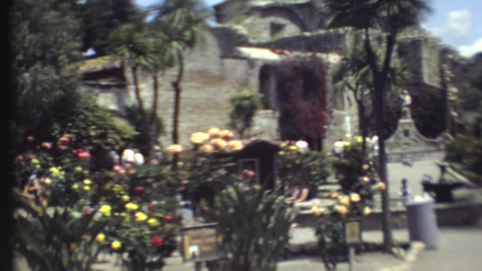 1972 8mm Grand Canyon garden view with stone architecture, flowering beds, palms, walkways, and distant visitors.
