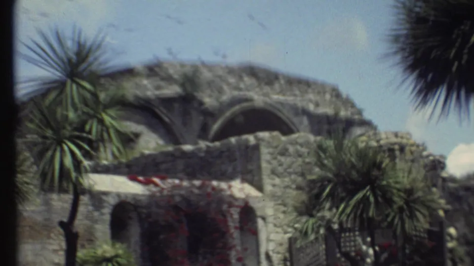 1972 8mm Grand Canyon-area travel footage showing a weathered stone structure framed by palm-like trees and flowering vines.