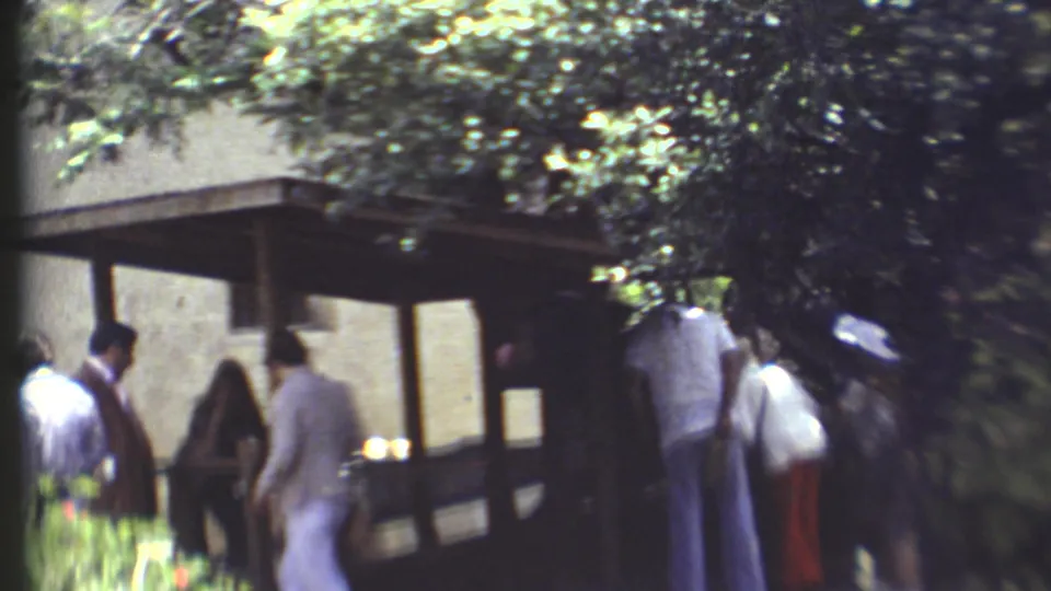 1972 Grand Canyon home-movie frame showing visitors walking near a wooden structure under leafy trees.