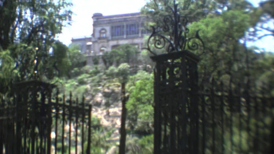 1973 Mexico City home-movie frame showing decorative iron gates, dense greenery, a rocky slope, and a large stone building on the hill.