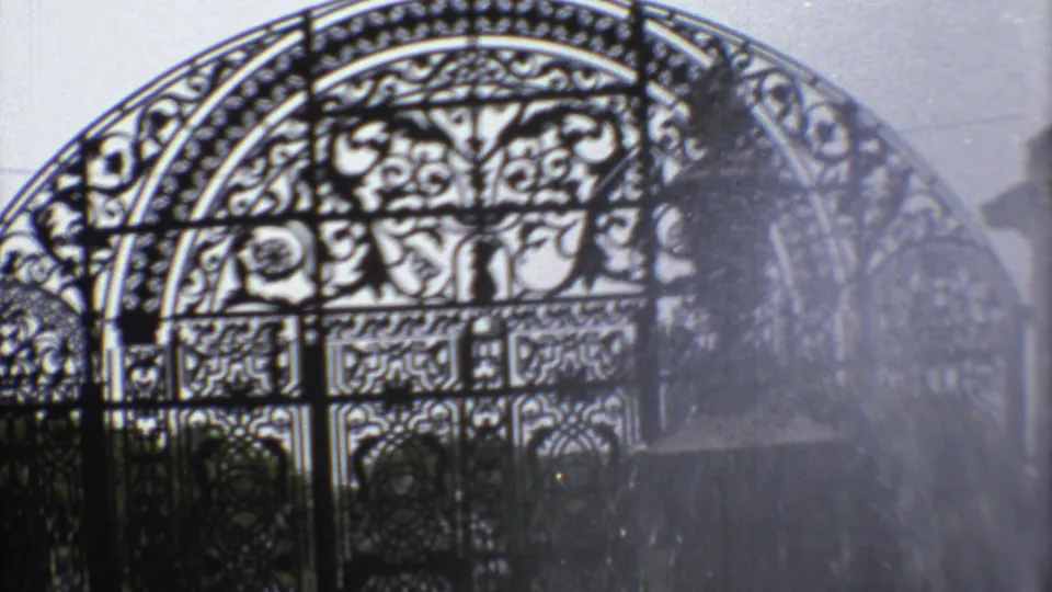 Ornate Mexico City garden gate on 8mm film, with fountain mist softening the metal scrollwork.