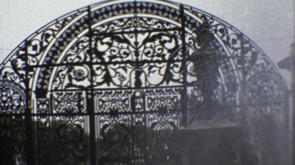1970s 8mm view of a decorative arched iron gate in Mexico City, filmed through bright fountain spray.