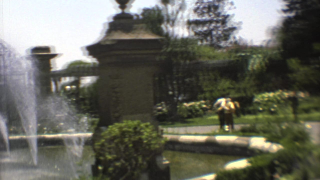 1973 Mexico City garden view with fountain basin, ornate pillars, clipped greenery, tropical plants, and a distant person near the walkway.