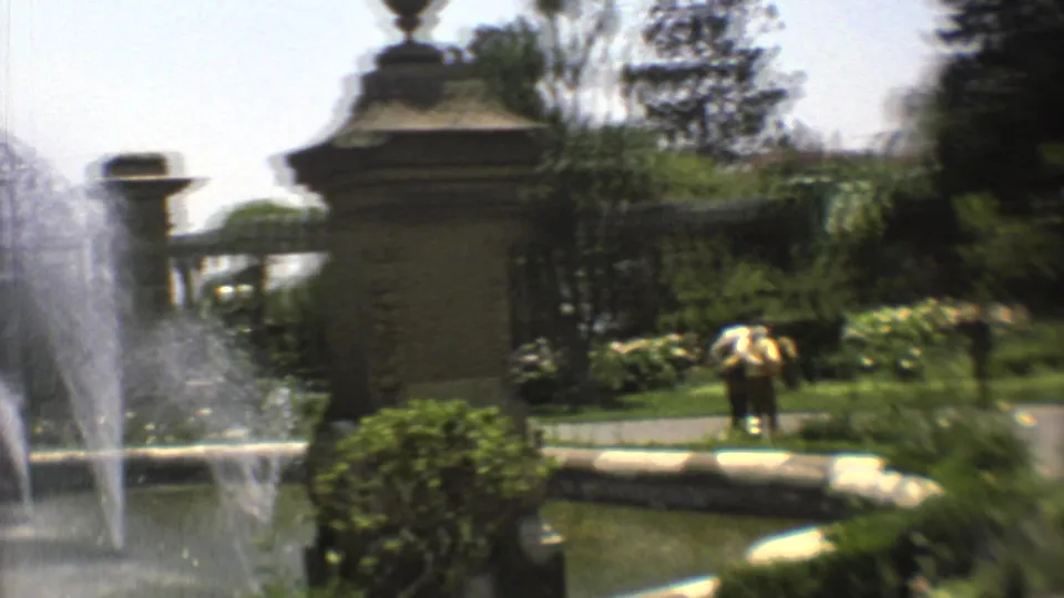 1973 Mexico City garden view with fountain basin, ornate pillars, clipped greenery, tropical plants, and a distant person near the walkway.