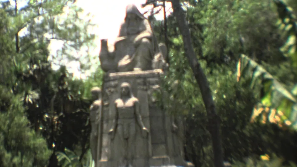 A closer 1973 garden frame shows a large stone statue or monument with carved human forms, surrounded by palms, trees, and sunlit greenery.