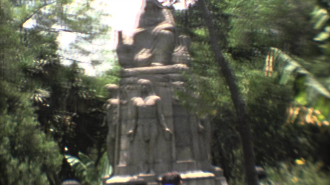 1973 Mexico City frame with carved stone figures seen through leafy garden foliage in soft 8mm color.
