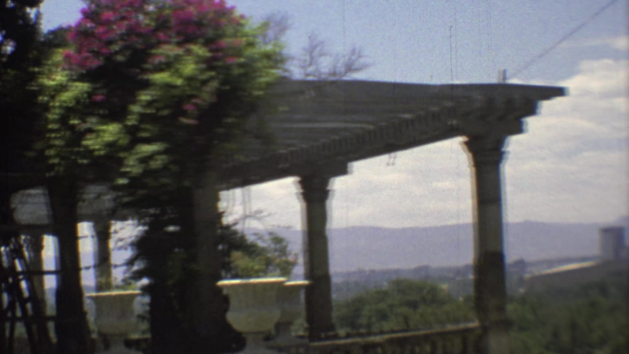 1973 Mexico City frame of a veranda with columns, railing, potted planter, foliage, and distant hills in hazy light.