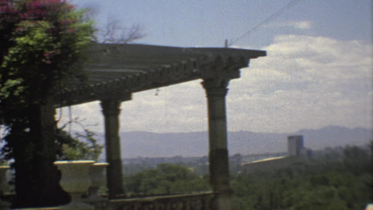 1973 Mexico City home-movie view from a stone porch, with columns, pergola, trees, distant buildings, and mountains.