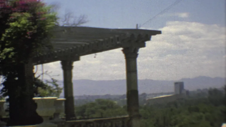 1973 Mexico City home-movie view from a stone porch, with columns, pergola, trees, distant buildings, and mountains.