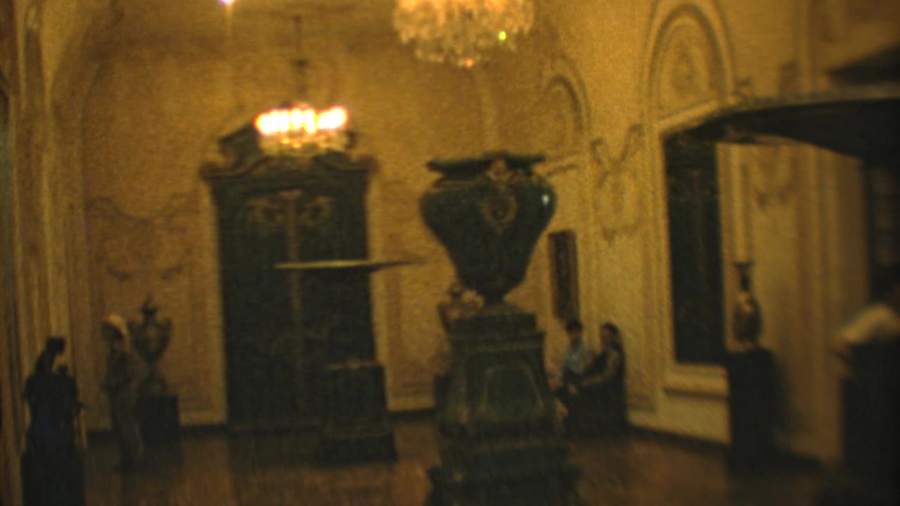 1973 Mexico City 8mm frame showing an ornate palace or museum room with chandeliers, carved furnishings, a large urn, and visitors.