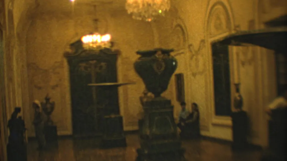 1973 Mexico City 8mm frame showing an ornate palace or museum room with chandeliers, carved furnishings, a large urn, and visitors.