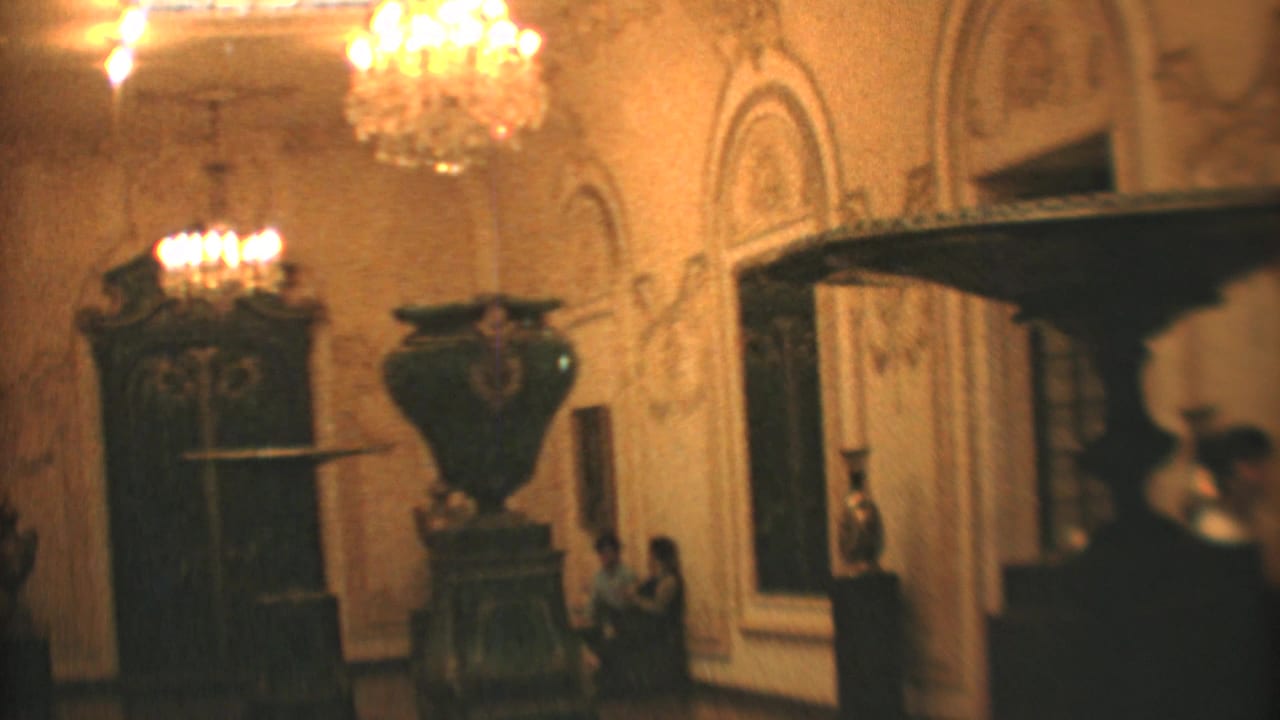 1973 Mexico City 8mm view of a formal interior with chandeliers, decorative wall detail, carved furniture, and passing visitors.