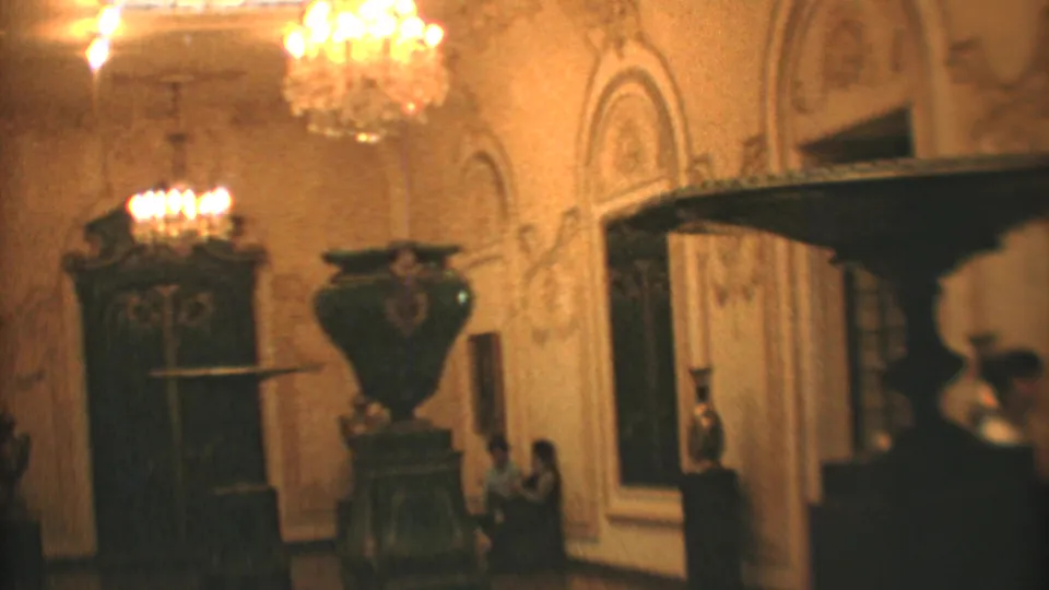 1973 Mexico City 8mm view of a formal interior with chandeliers, decorative wall detail, carved furniture, and passing visitors.