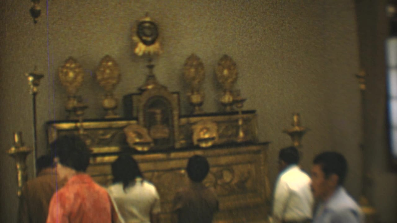 1973 Mexico City 8mm frame showing people viewed from behind before a gilded church altar with candles and religious figures.