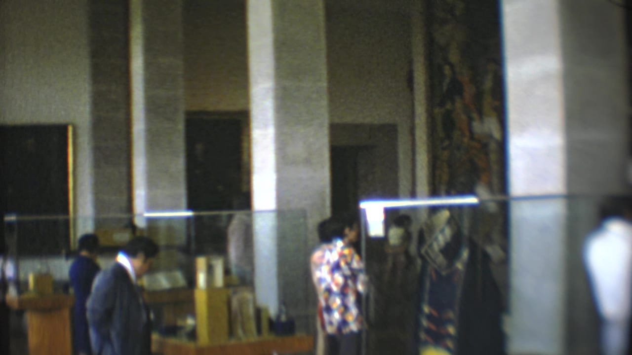 A man in a dark suit and another in a patterned shirt stand near display cases.