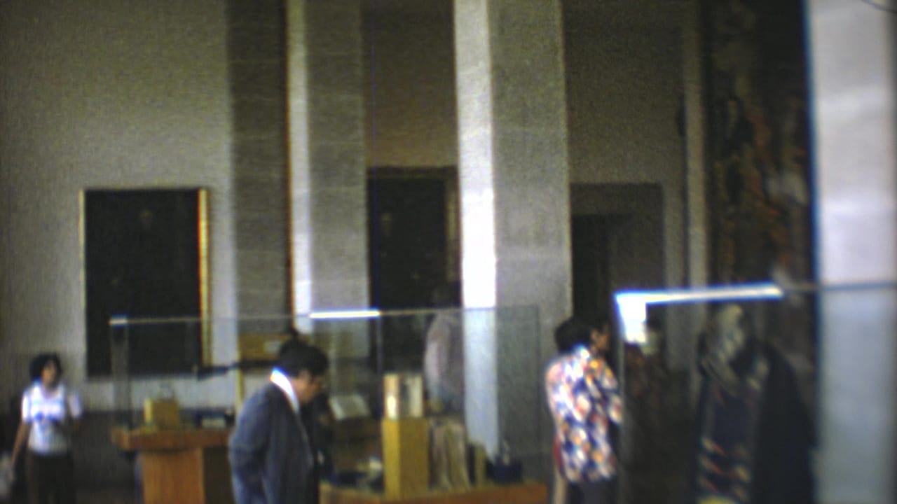 Museum visitors in Mexico City appear inside a tall hall with display cases, stone columns, and a dark framed wall feature.