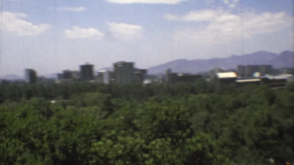 Mexico City skyline appears across the horizon beyond trees, with distant mountains under a bright partly cloudy sky.