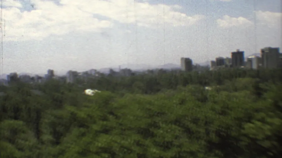End of the panoramic view shows Mexico City towers to the right, green canopy below, and hazy mountains beneath a bright sky.