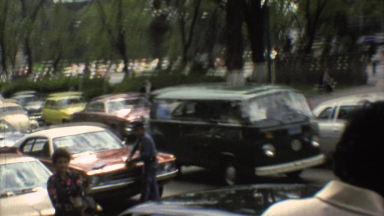 Parked cars and pedestrians along a tree-lined city street with a green van in traffic.