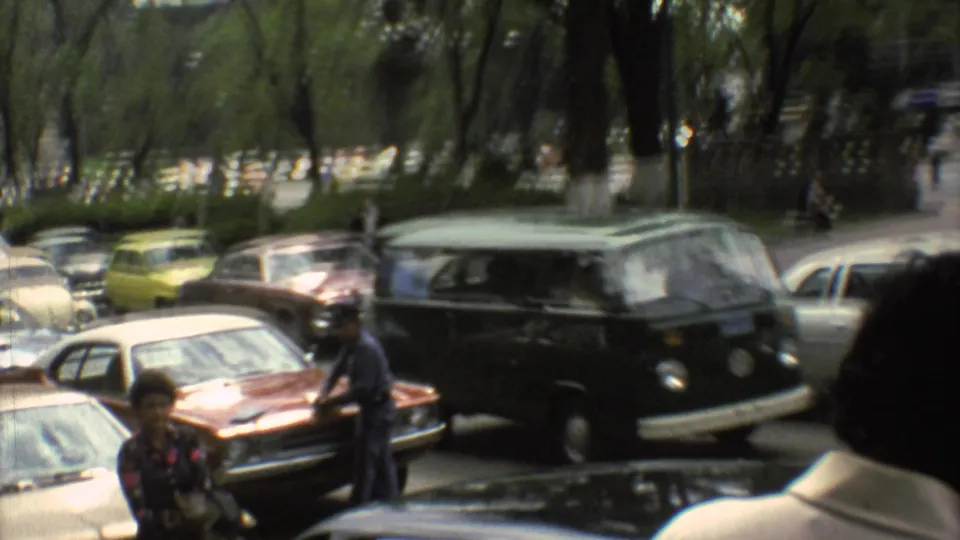 1973 Mexico City street view with parked sedans, pedestrians, mature trees, and a dark green van moving through traffic.