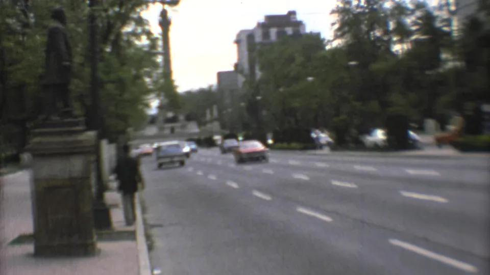 1973 Mexico City home-movie view of traffic on a broad avenue beside trees, pedestrians, and part of a stone monument.