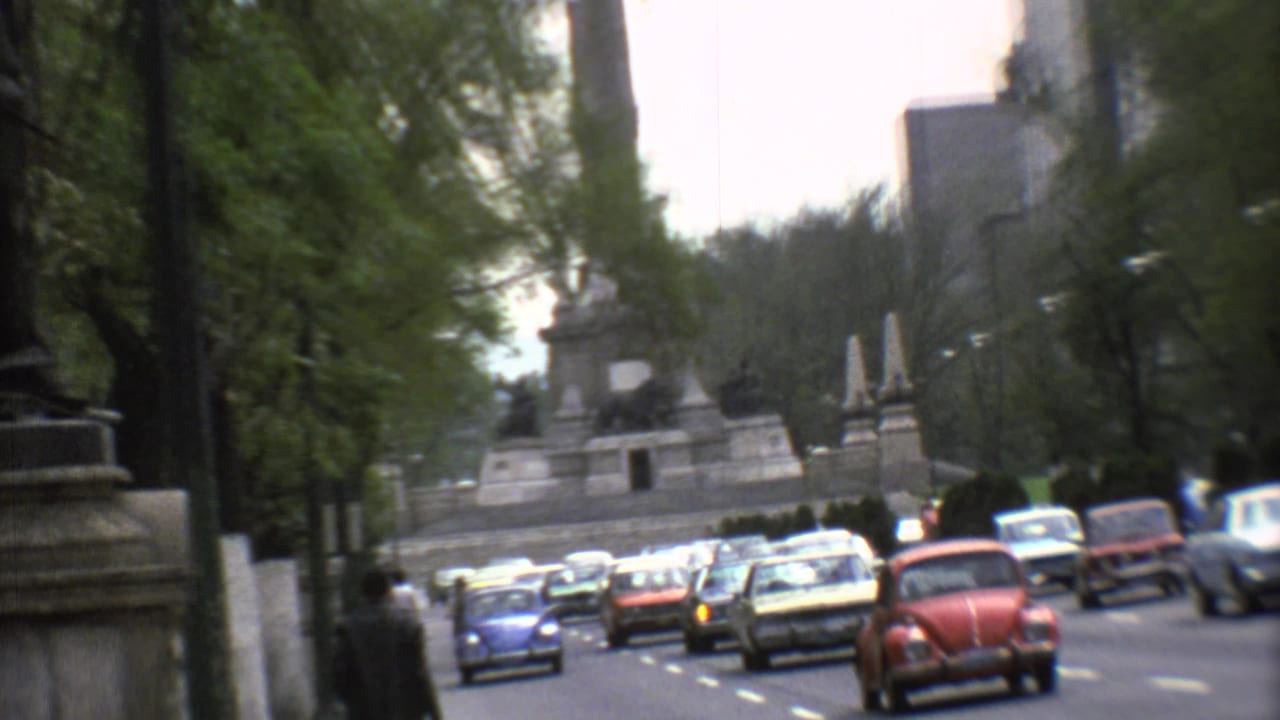 Mexico City avenue in 1973 with the monument set back beyond rows of classic cars and roadside trees.