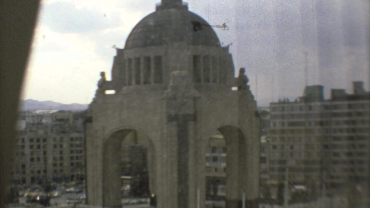 Monumento a la Revolución seen through a window with surrounding city buildings and sky.