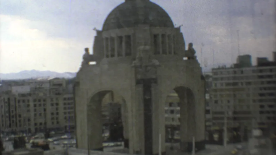 A 1973 home-movie frame shows the Mexico City monument from a windowed vantage, with mid-century buildings and mountains behind it.