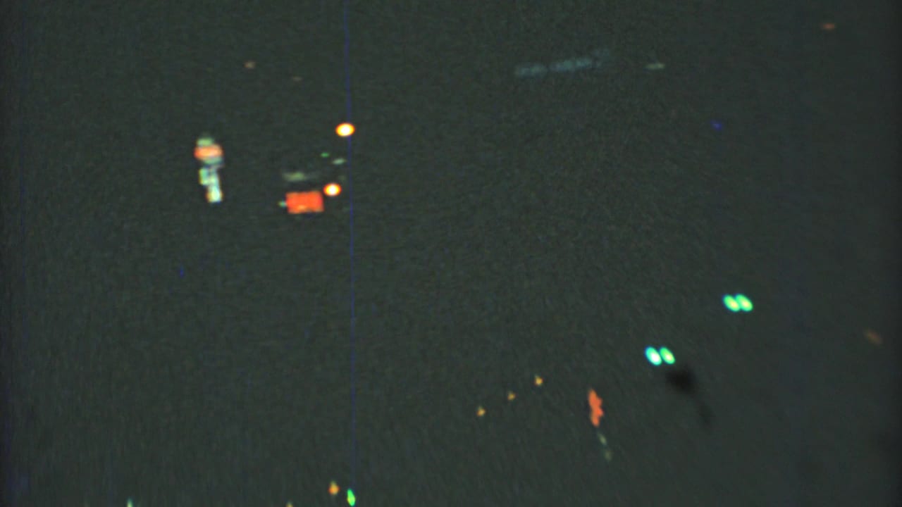 Dark street view with distant red, green, and orange lights against a grainy night frame.