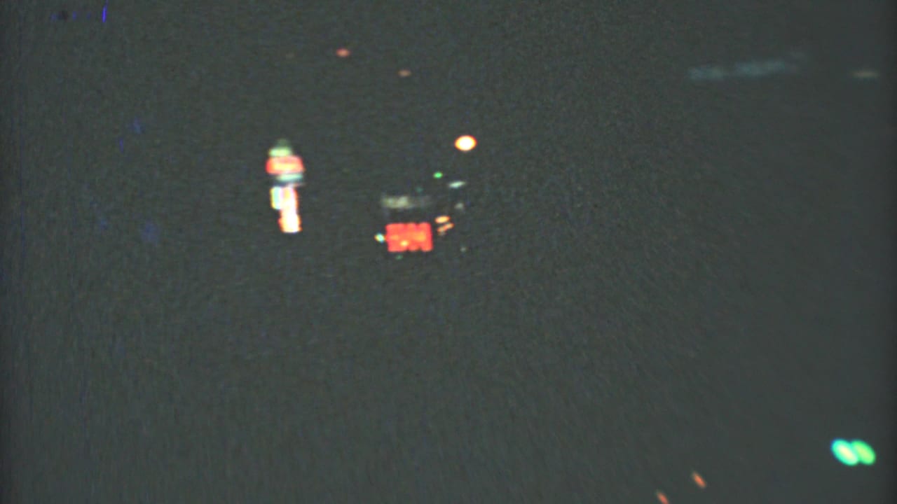 1973 8mm Mexico City street view at night, with blurred red signage and small green lights seen from a moving vehicle.