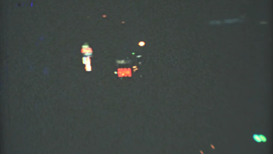 1973 8mm Mexico City street view at night, with blurred red signage and small green lights seen from a moving vehicle.