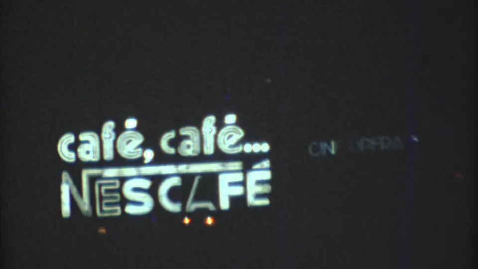 1973 Mexico City night frame showing a close view of illuminated cafe and Nescafe advertising signage.