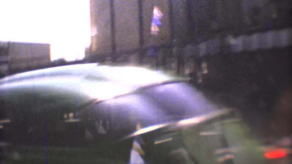 1973 Mexico City moving-car view with reflected glare, a vehicle edge, and blurred nighttime street forms.