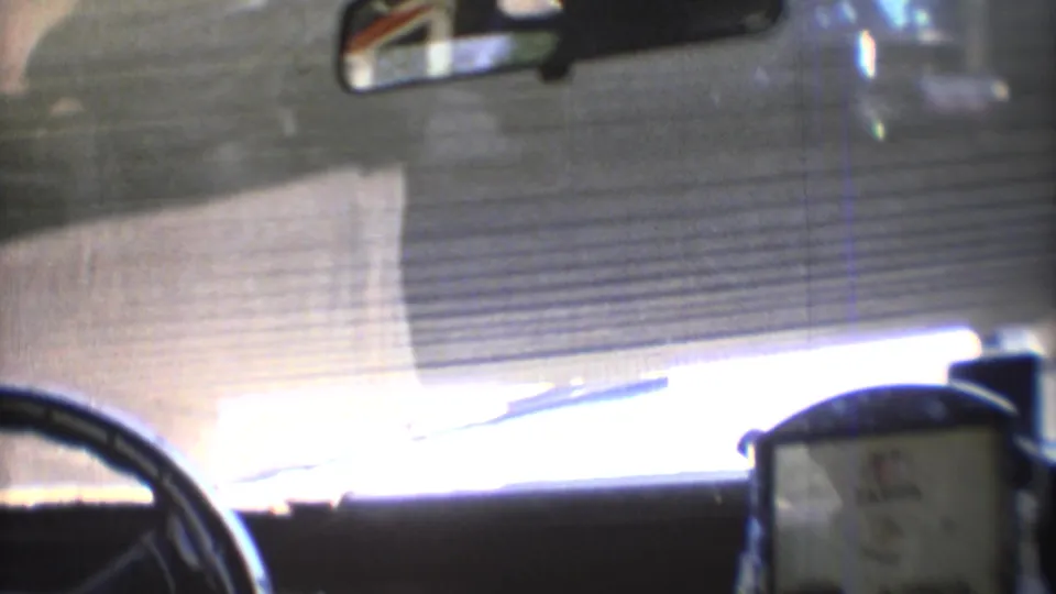 Interior 8mm view from a car in 1973 Mexico City, showing windshield glare, a rearview mirror, dashboard area, and road surface outside.