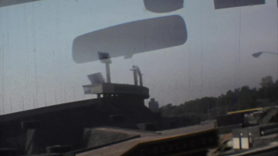 1973 Mexico City 8mm frame showing a stadium exterior, floodlight tower and windshield edge from a moving vehicle.