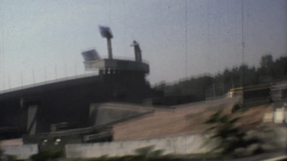 1973 Mexico City home-movie frame of a large stadium exterior with floodlights and paved approaches under bright sun.