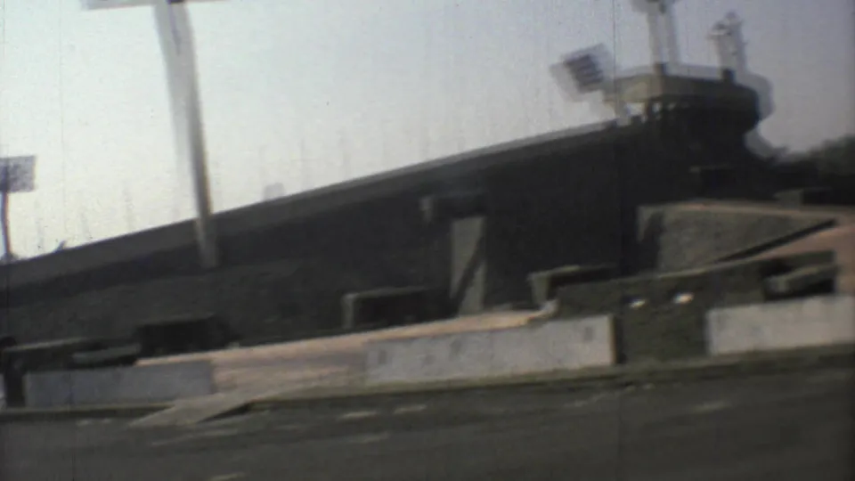 1973 Mexico City 8mm frame with a closer drive-by angle on the stadium, a light pole and empty pavement.