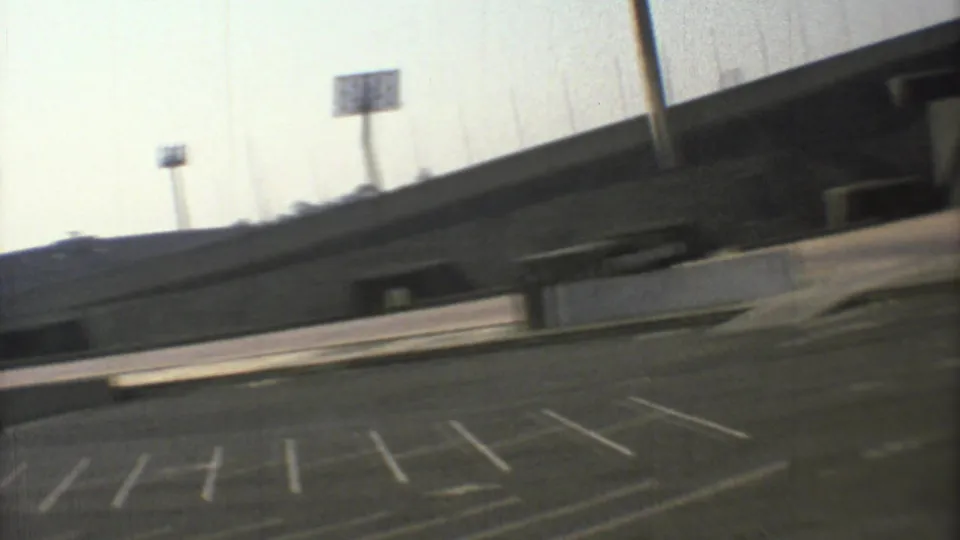 1973 Mexico City frame showing the stadium edge, floodlights and an empty striped parking lot in the foreground.