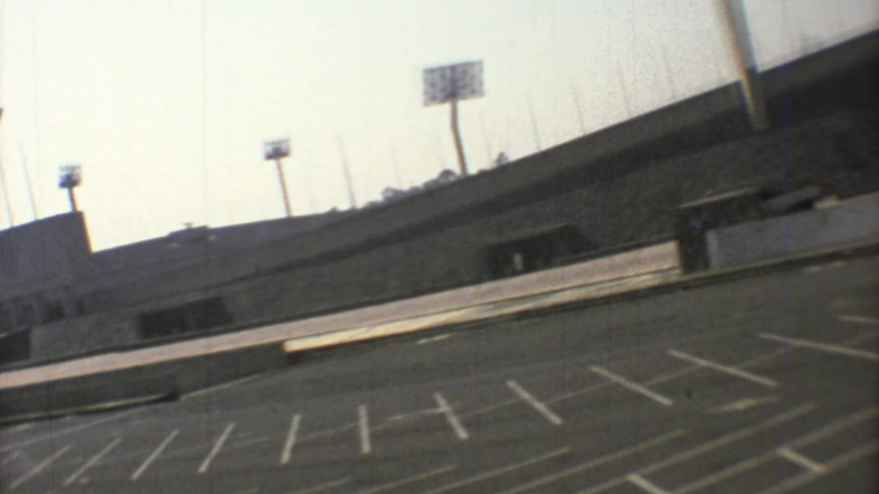 Empty marked parking lot beside a curved stadium exterior with floodlights.