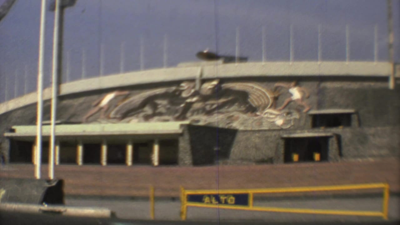 Modern building facade with sports mural, flagpoles, and yellow ALTO barrier.
