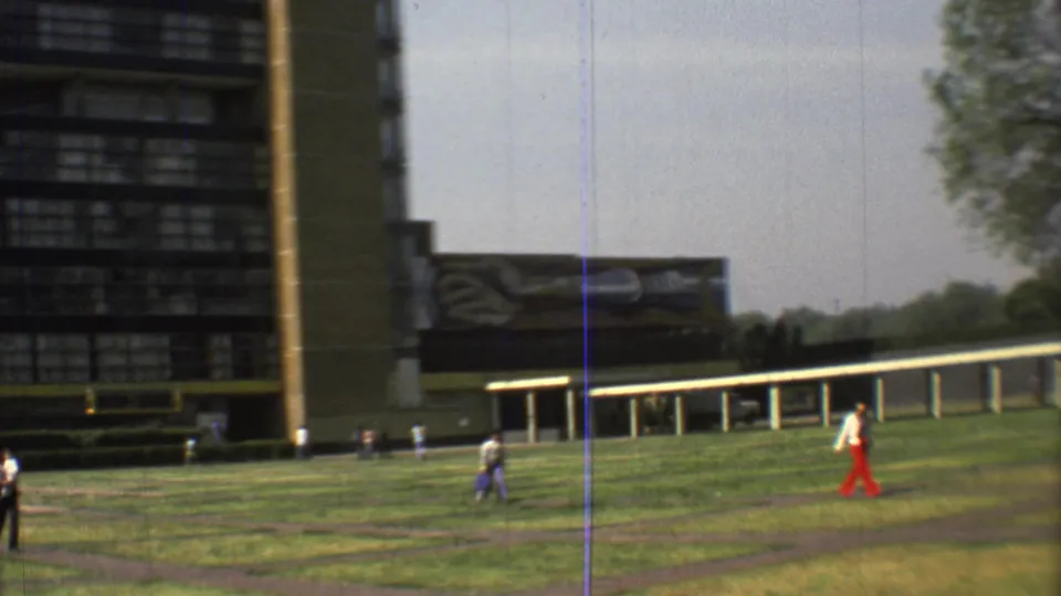1973 Mexico City 8mm frame of pedestrians moving through a campus-like lawn beside a tall modern building and covered walkway.