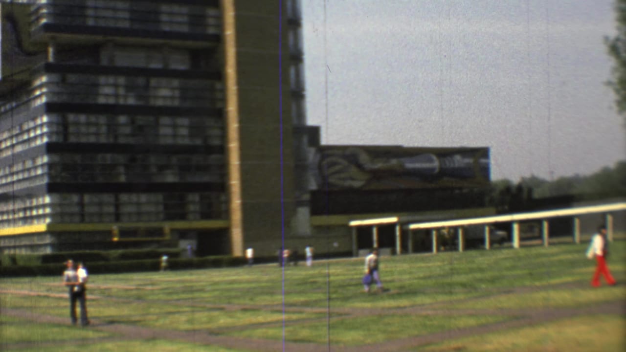 Dark multistory building beside a grassy lawn with pedestrians and a path.