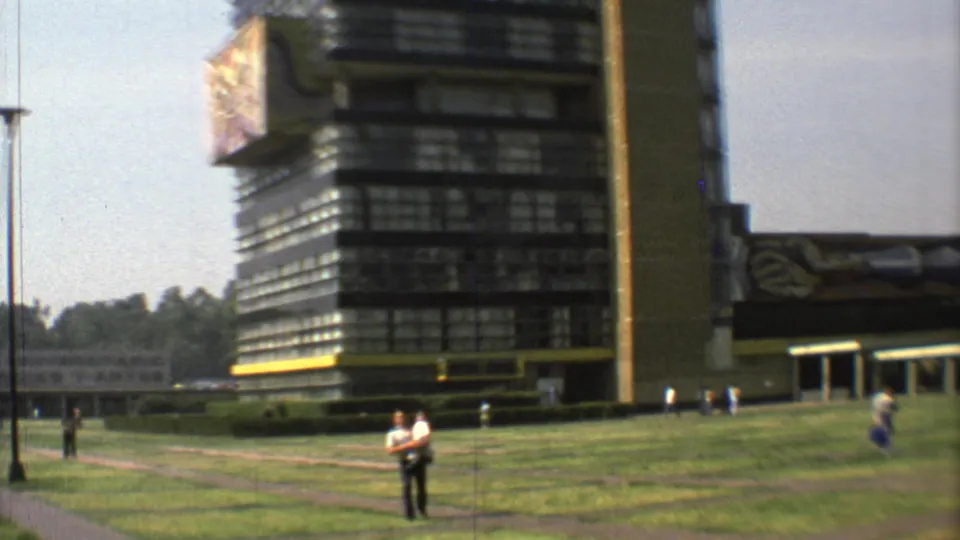 1973 Mexico City view of the modern building with a decorative protrusion, open grass and pedestrians near the path.