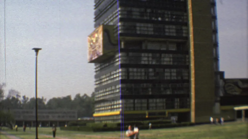 Soft 8mm frame of a Mexico City modernist building with yellow accents, a lawn, lamp post and distant pedestrians.