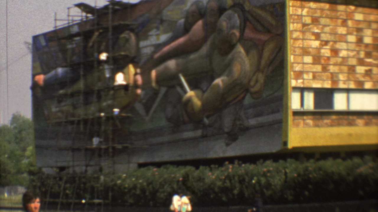 1973 Mexico City view of a monumental mural on a building facade, with scaffolding and lamps in front of painted figures.