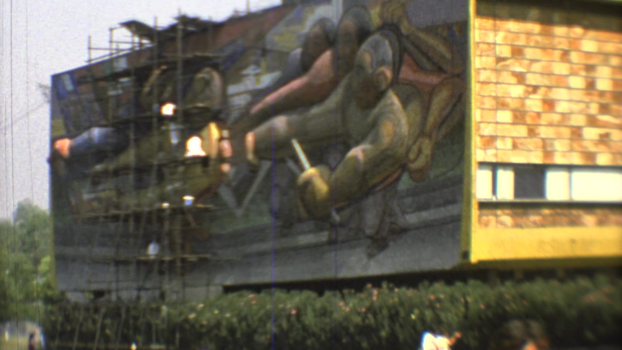 Modernist building with a large mural under scaffolding beside a lawn.