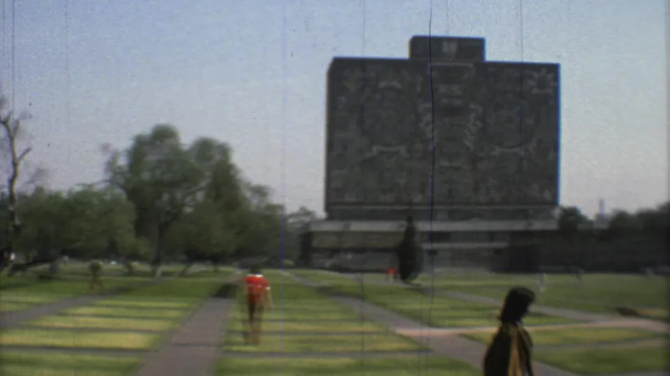 1973 Mexico City 8mm frame showing a large carved stone monument beyond lawns, paths, trees, and several distant pedestrians.