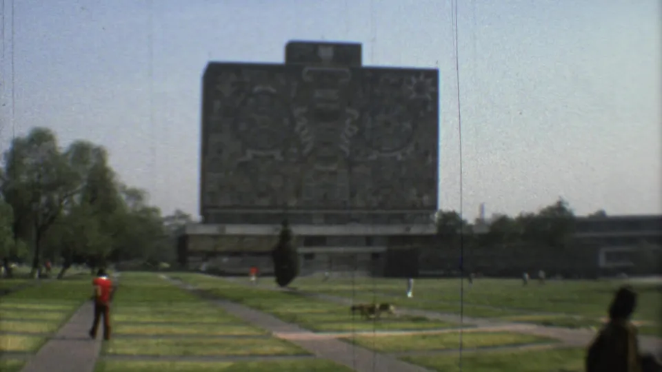 1973 Mexico City park view with a man in a red shirt on a walkway, a large stone monument, open grass, trees, and distant visitors.